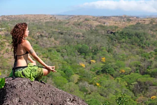 Woman meditating on top of a rock admiring the landscape