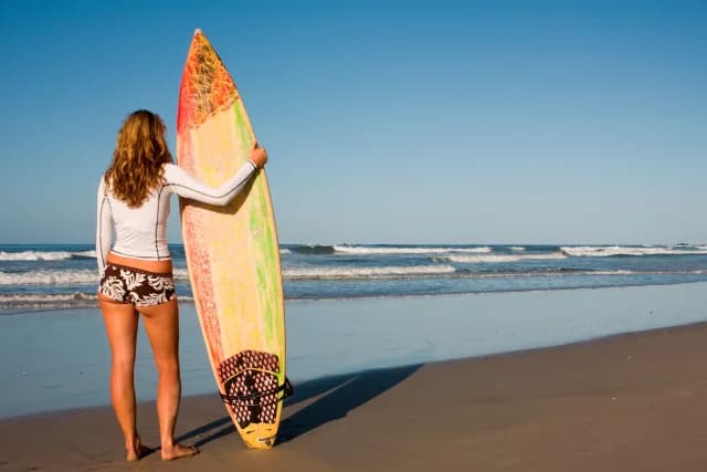 Girl standing on Avellanas beach with her surfing board, ready to take the waves